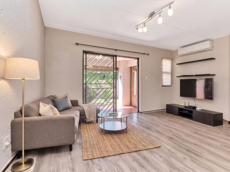 A well-maintained living room featuring laminate flooring, track lighting, a wall-mounted air conditioner, and sliding glass doors providing access to the patio.