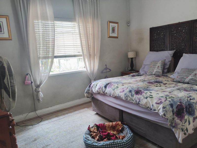 A bedroom featuring a window with venetian blinds and skirting boards. The room shows signs of wear including wall staining and scuffed paint.