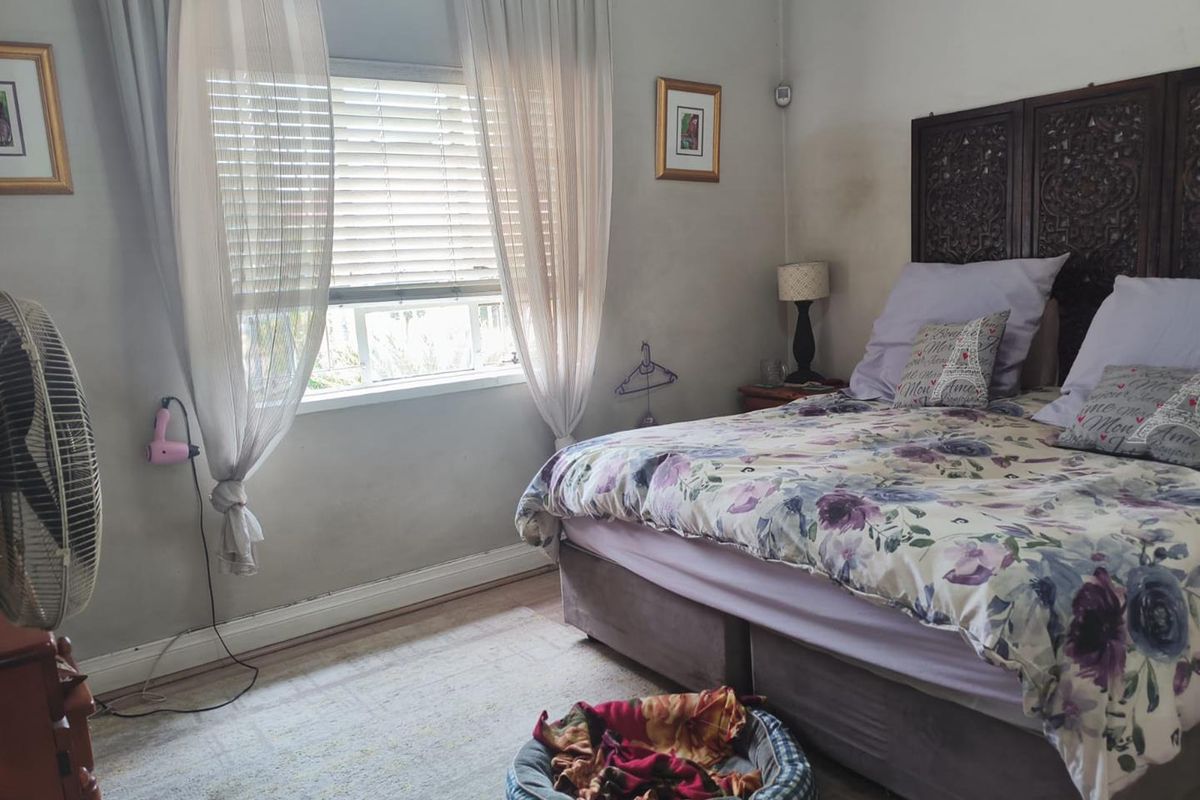 A bedroom featuring a window with venetian blinds and skirting boards. The room shows signs of wear including wall staining and scuffed paint.