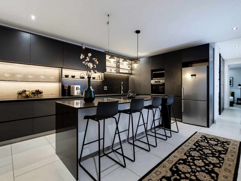 Modern kitchen featuring sleek dark cabinetry, a central island with breakfast bar seating, integrated appliances, and sophisticated under-cabinet lighting.