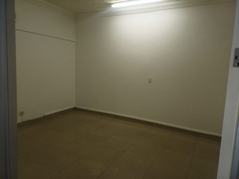 A vacant, neutral office space featuring tiled flooring and overhead fluorescent lighting, providing a clean and functional environment for professional use.