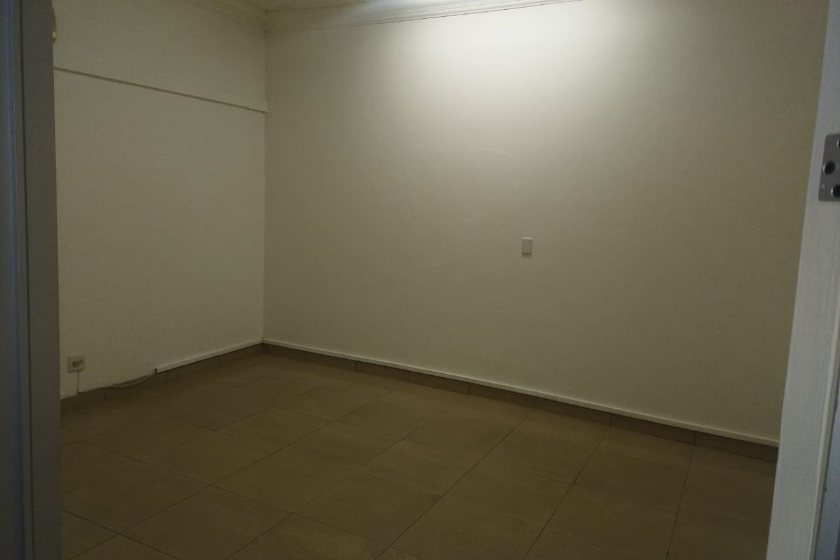 A vacant, neutral office space featuring tiled flooring and overhead fluorescent lighting, providing a clean and functional environment for professional use.