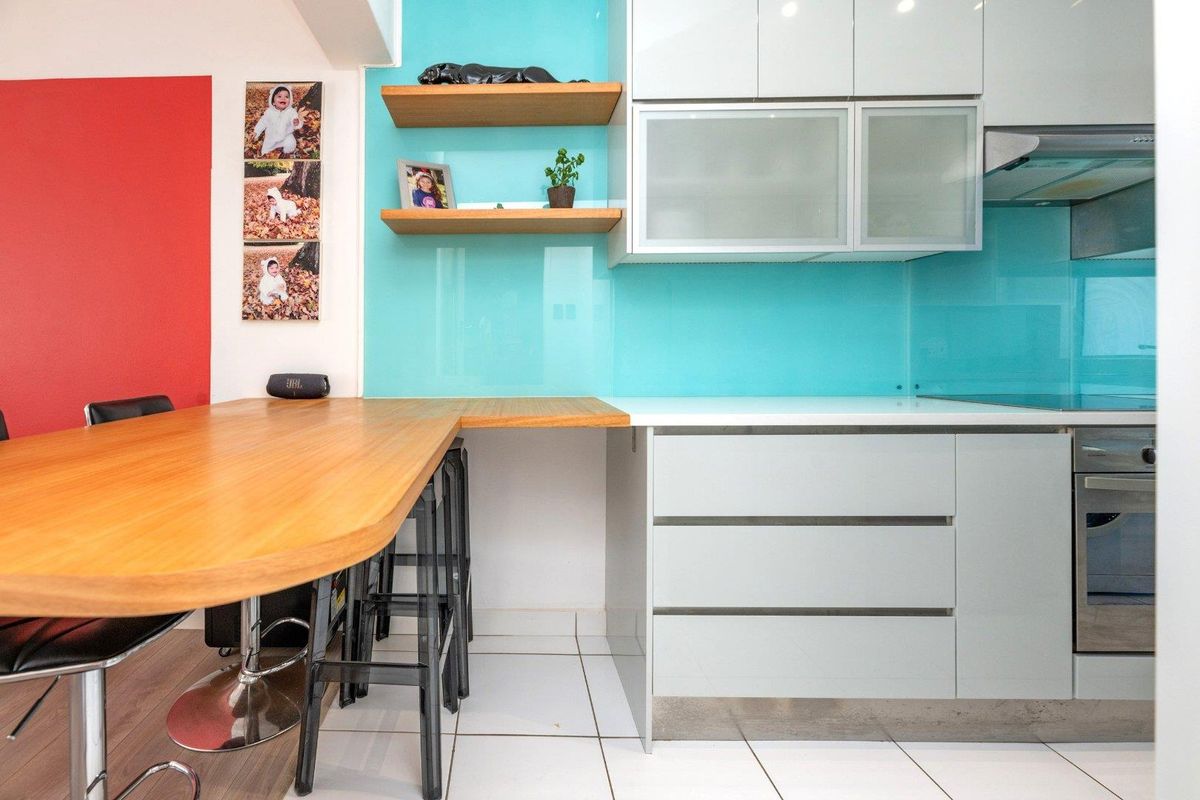Modern kitchen featuring sleek cabinetry, a vibrant glass splashback, built-in oven, extractor fan, and a functional integrated breakfast bar with floating shelving.