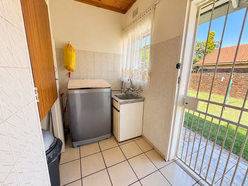 Functional laundry area featuring a stainless steel sink, tiled splashbacks, and direct access to the rear garden through a secure gate.