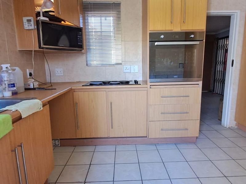 A functional kitchen featuring light wood-finish cabinetry, built-in oven and hob, tiled flooring, and a stainless steel sink with tiled backsplash.