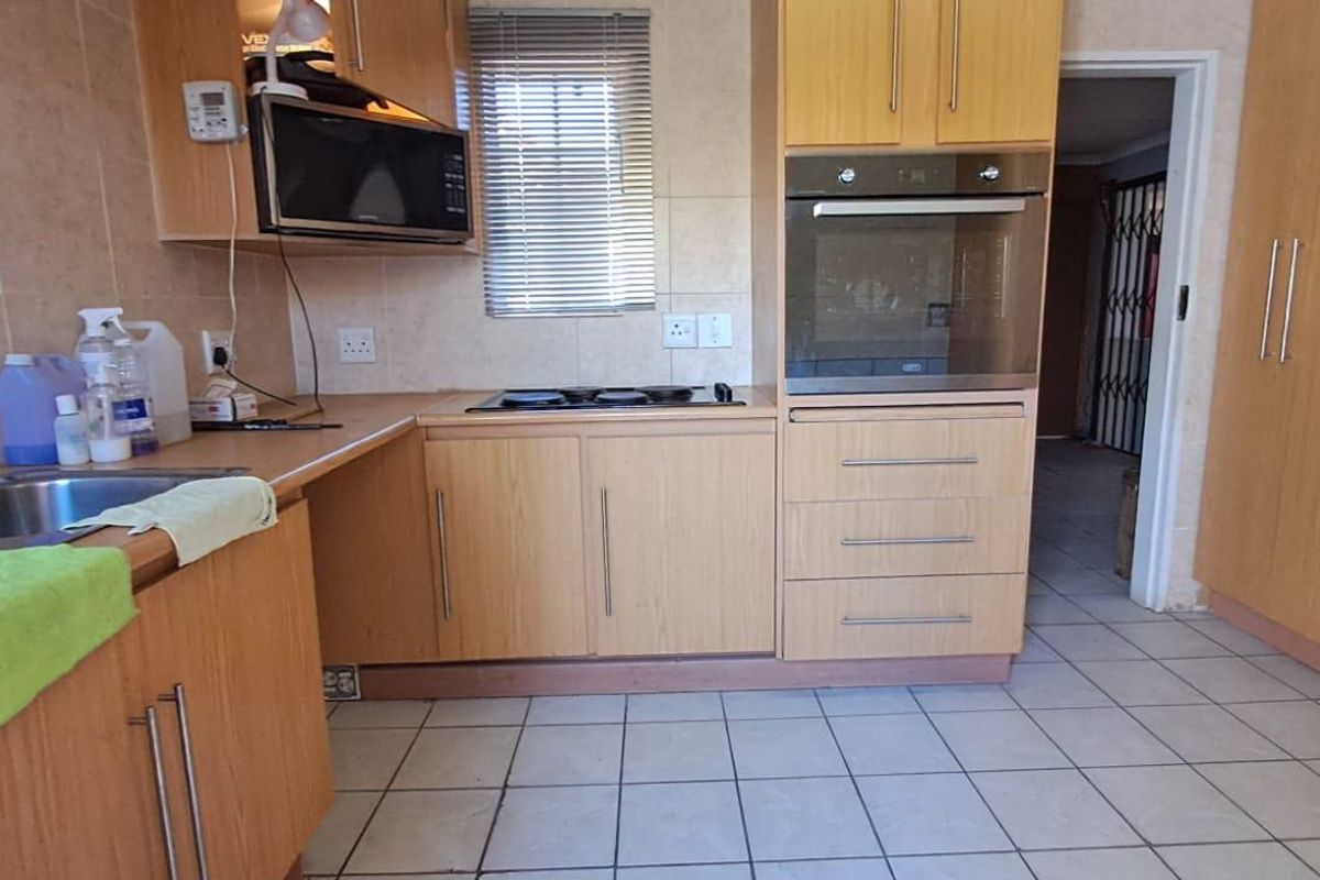 A functional kitchen featuring light wood-finish cabinetry, built-in oven and hob, tiled flooring, and a stainless steel sink with tiled backsplash.