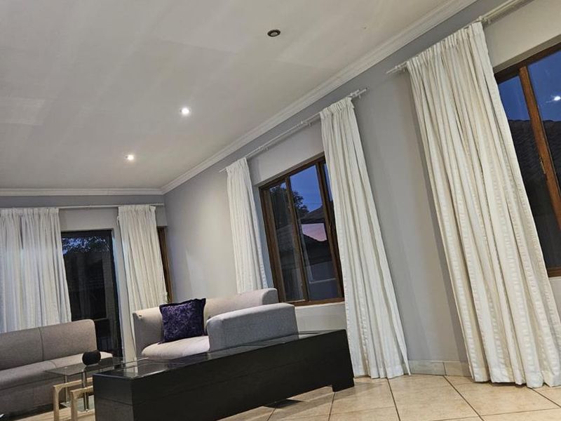 Spacious living room featuring neutral tiled flooring, recessed downlighting, and large windows with timber frames, offering a bright and open atmosphere.