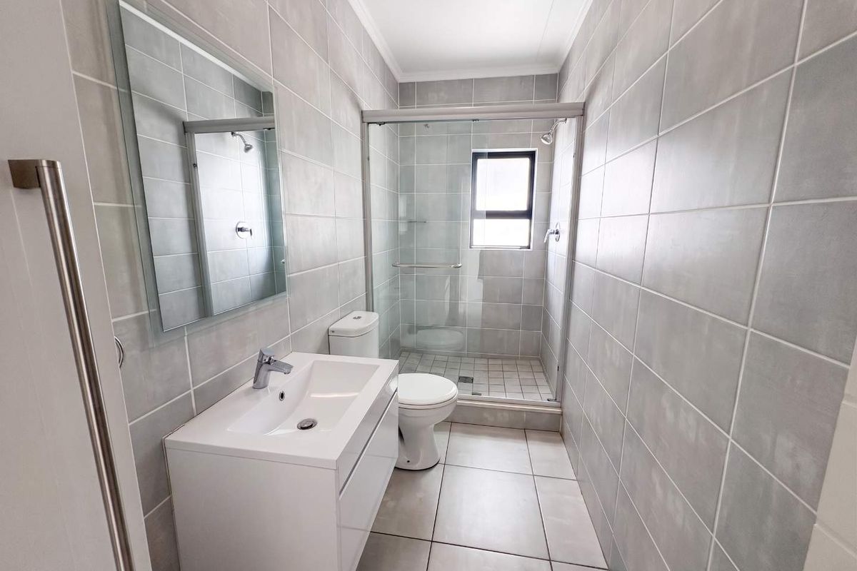 Modern bathroom featuring grey wall and floor tiles, a white vanity with basin, a toilet, and a glass-enclosed shower.