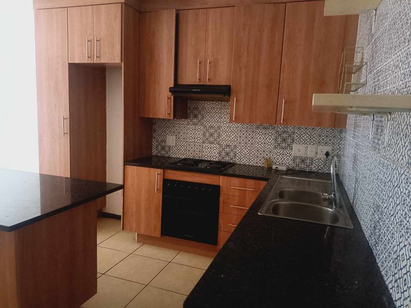 A functional kitchen featuring wood-look cabinetry, granite countertops, a built-in oven with extractor fan, and a decorative patterned tile backsplash.