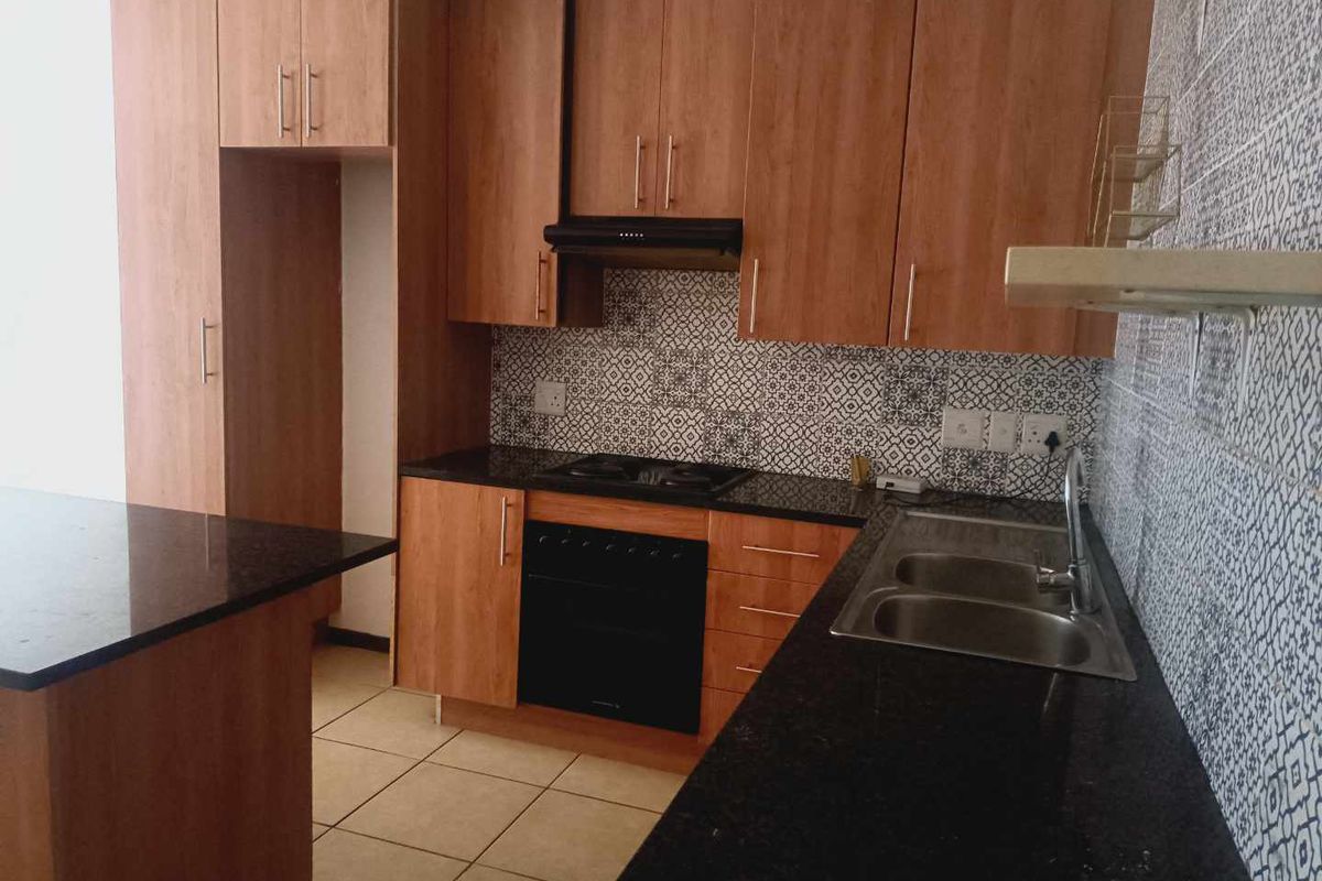 A functional kitchen featuring wood-look cabinetry, granite countertops, a built-in oven with extractor fan, and a decorative patterned tile backsplash.