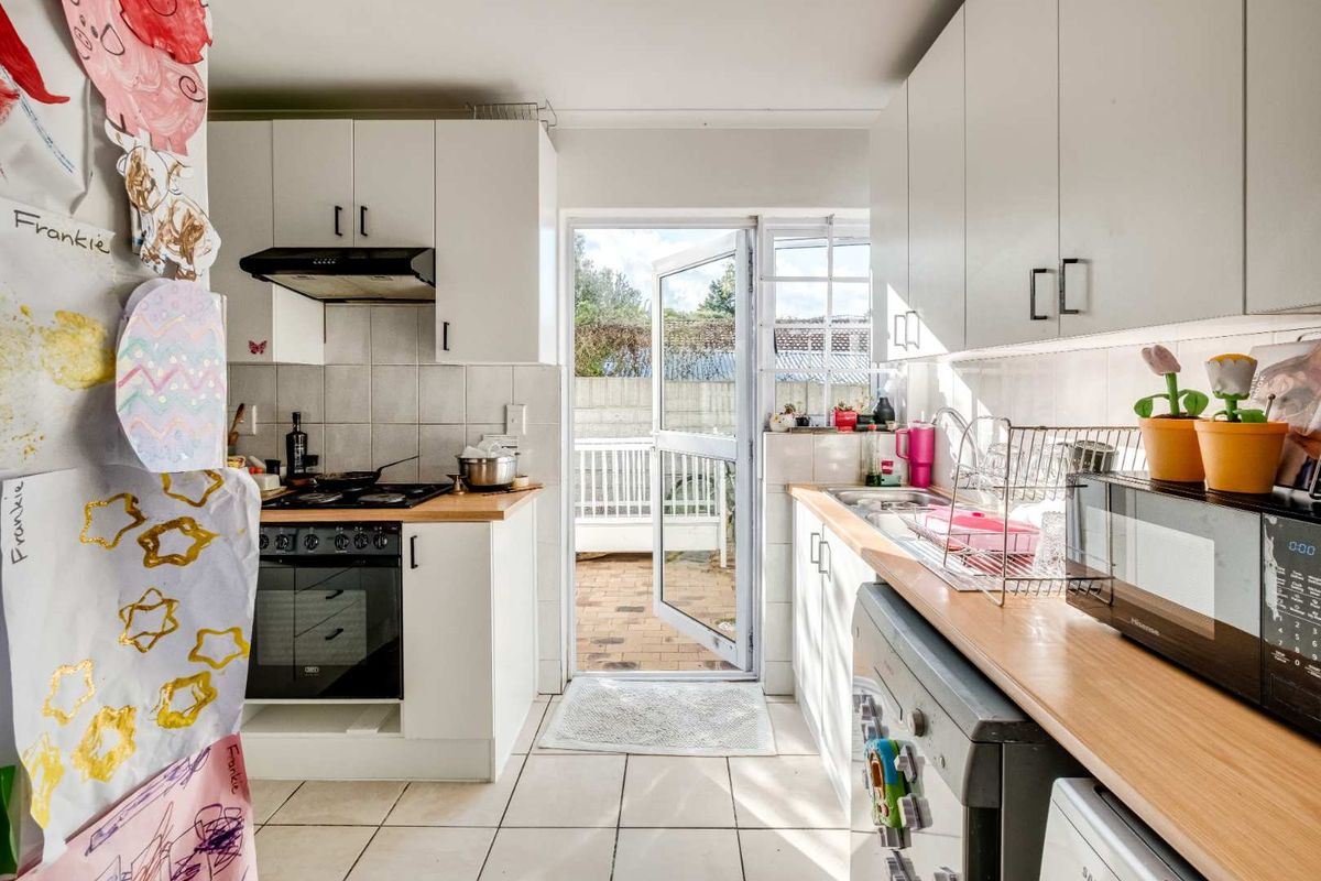 Functional kitchen featuring white cabinetry, wood-look countertops, built-in oven and hob, and direct access to an outdoor patio area.