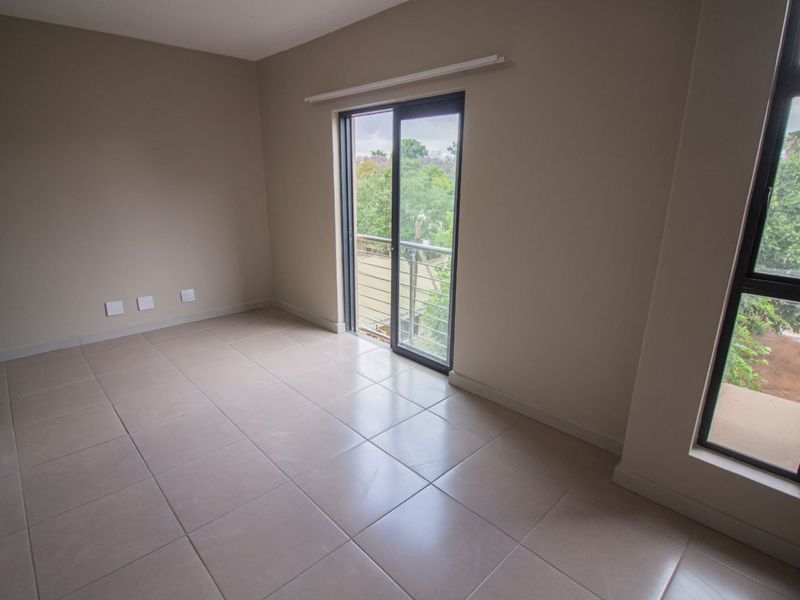 A bright, empty bedroom featuring neutral tiled flooring, large windows, and a sliding glass door providing access to a private balcony.