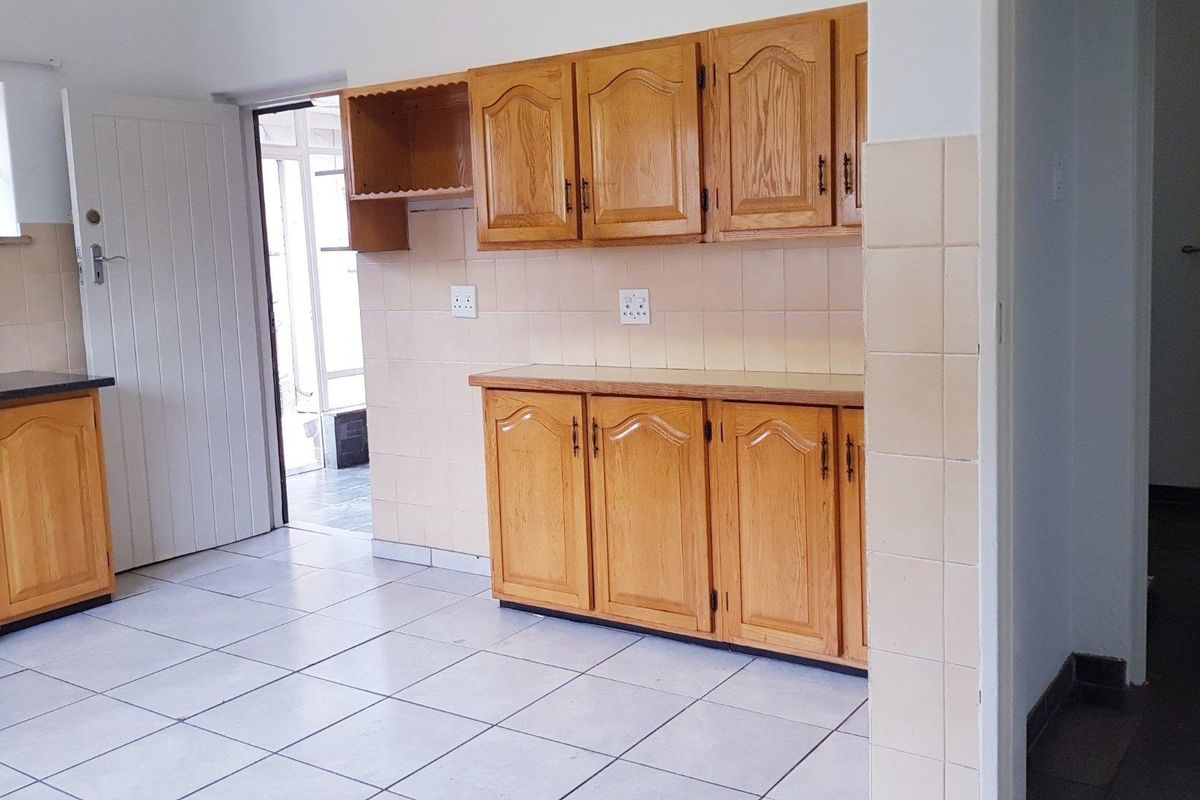 A functional kitchen featuring wooden cabinetry, tiled flooring, and a tiled backsplash, offering a clean and empty space ready for updates.