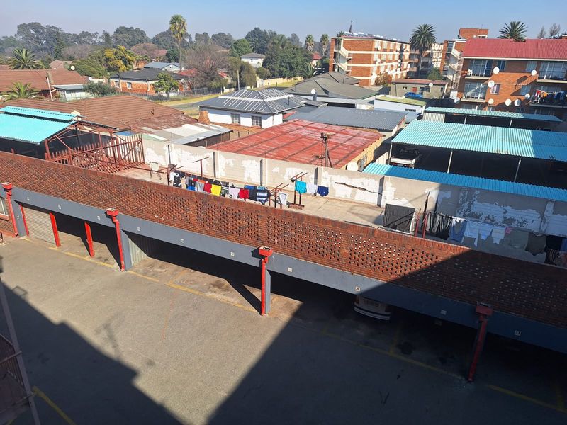 Elevated view of the apartment complex parking area featuring covered bays, brick boundary walls, and surrounding residential neighborhood infrastructure.