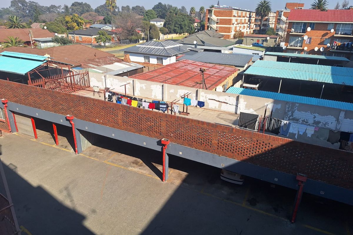 Elevated view of the apartment complex parking area featuring covered bays, brick boundary walls, and surrounding residential neighborhood infrastructure.