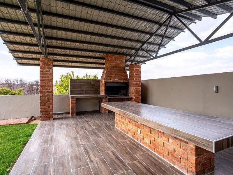 Covered outdoor patio featuring a built-in brick braai, tiled prep surfaces, and durable wood-look floor tiles, ideal for alfresco dining and entertainment.