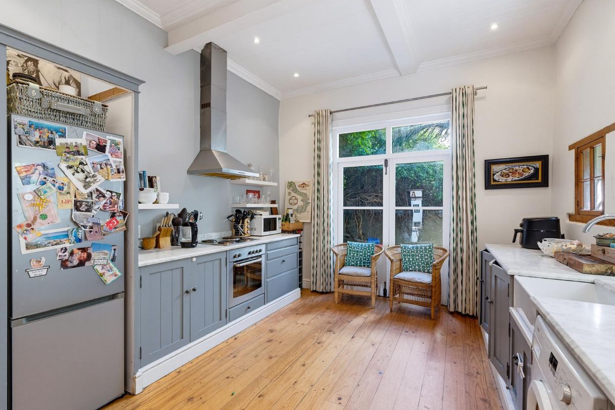 A charming kitchen featuring grey cabinetry, marble countertops, a farmhouse sink, and warm timber flooring, with direct access to the garden.