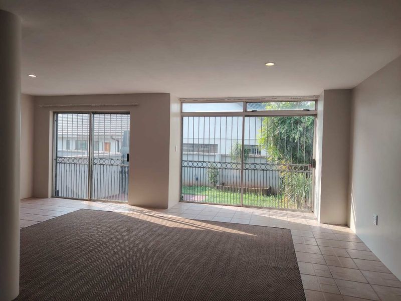 Spacious living area featuring large sliding glass doors with security bars, recessed lighting, and neutral tiled flooring, offering direct access to the rear garden.