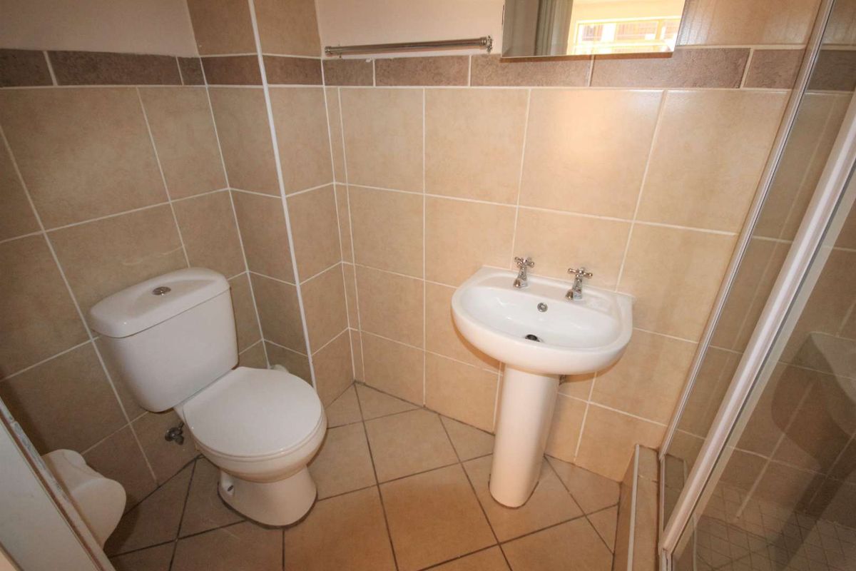 A functional bathroom featuring a pedestal washbasin, dual flush toilet, and a shower enclosure with neutral ceramic tiling throughout.