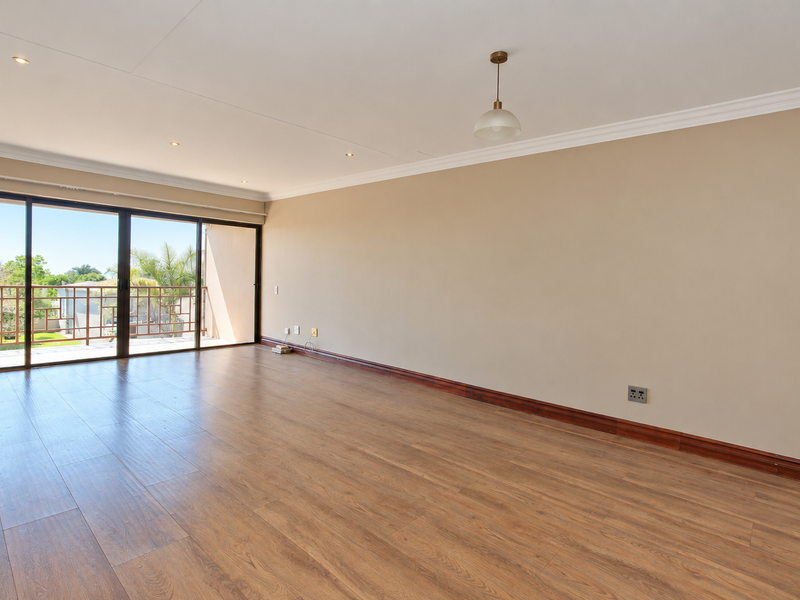 A spacious, empty living room featuring laminate flooring, recessed lighting, and large sliding glass doors that open onto a balcony.
