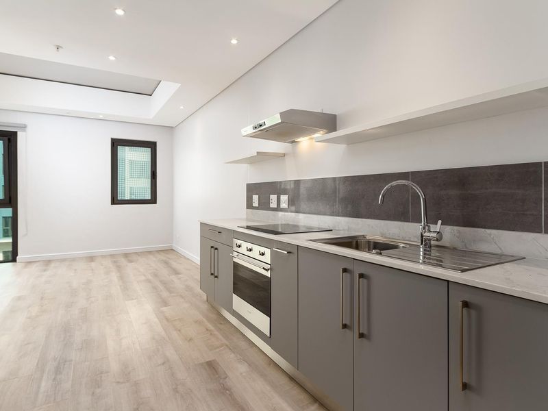 Modern, minimalist kitchen featuring sleek grey cabinetry, stone countertops, integrated appliances, and recessed lighting in an open-plan layout.
