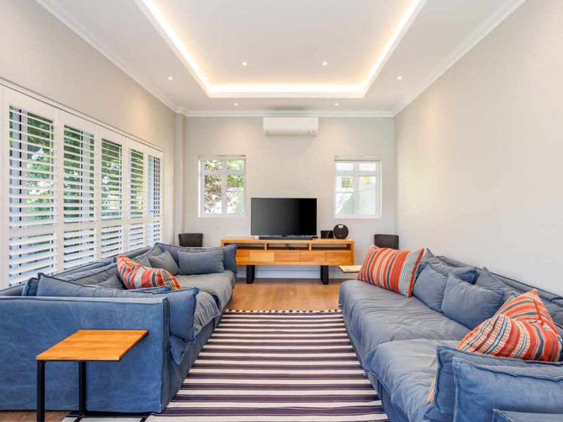 A bright and modern living room featuring timber flooring, recessed cove lighting, split-system air conditioning, and white plantation shutters.