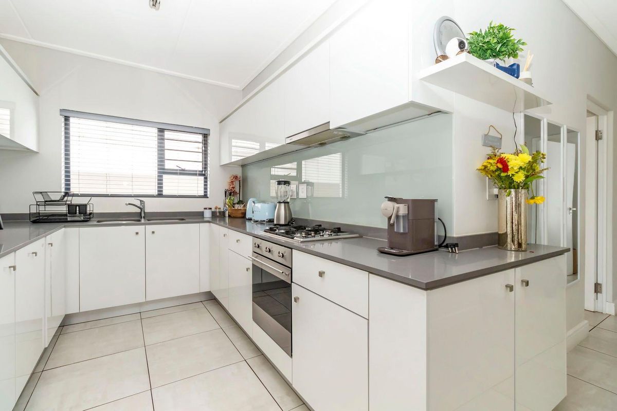 Modern kitchen featuring white cabinetry, stone countertops, a glass splashback, built-in oven, gas hob, and stainless steel sink.
