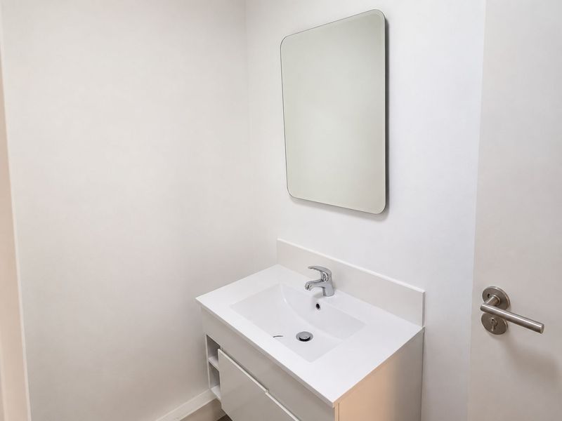 A clean and modern bathroom featuring a white vanity cabinet with an integrated sink, chrome faucet, and a simple wall-mounted mirror.