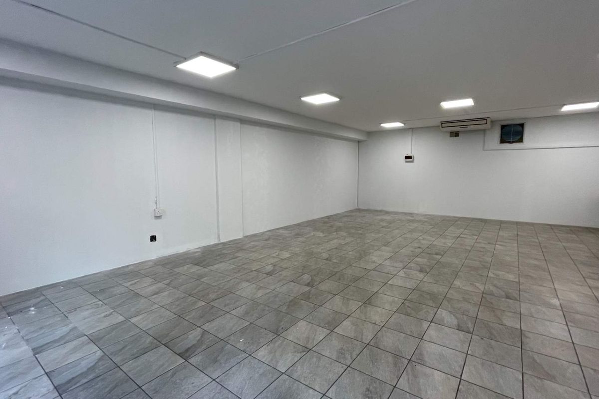 A spacious, empty open-plan retail area featuring neutral ceramic floor tiles, recessed LED lighting, and a wall-mounted air conditioning unit.