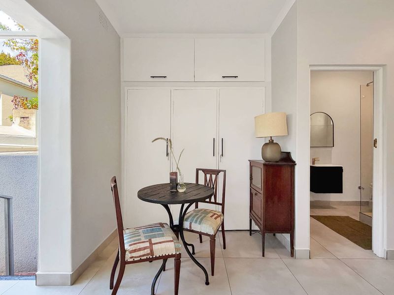 A bright living area featuring built-in floor-to-ceiling cupboards, neutral tiled flooring, and direct access to an adjacent bathroom and outdoor space.
