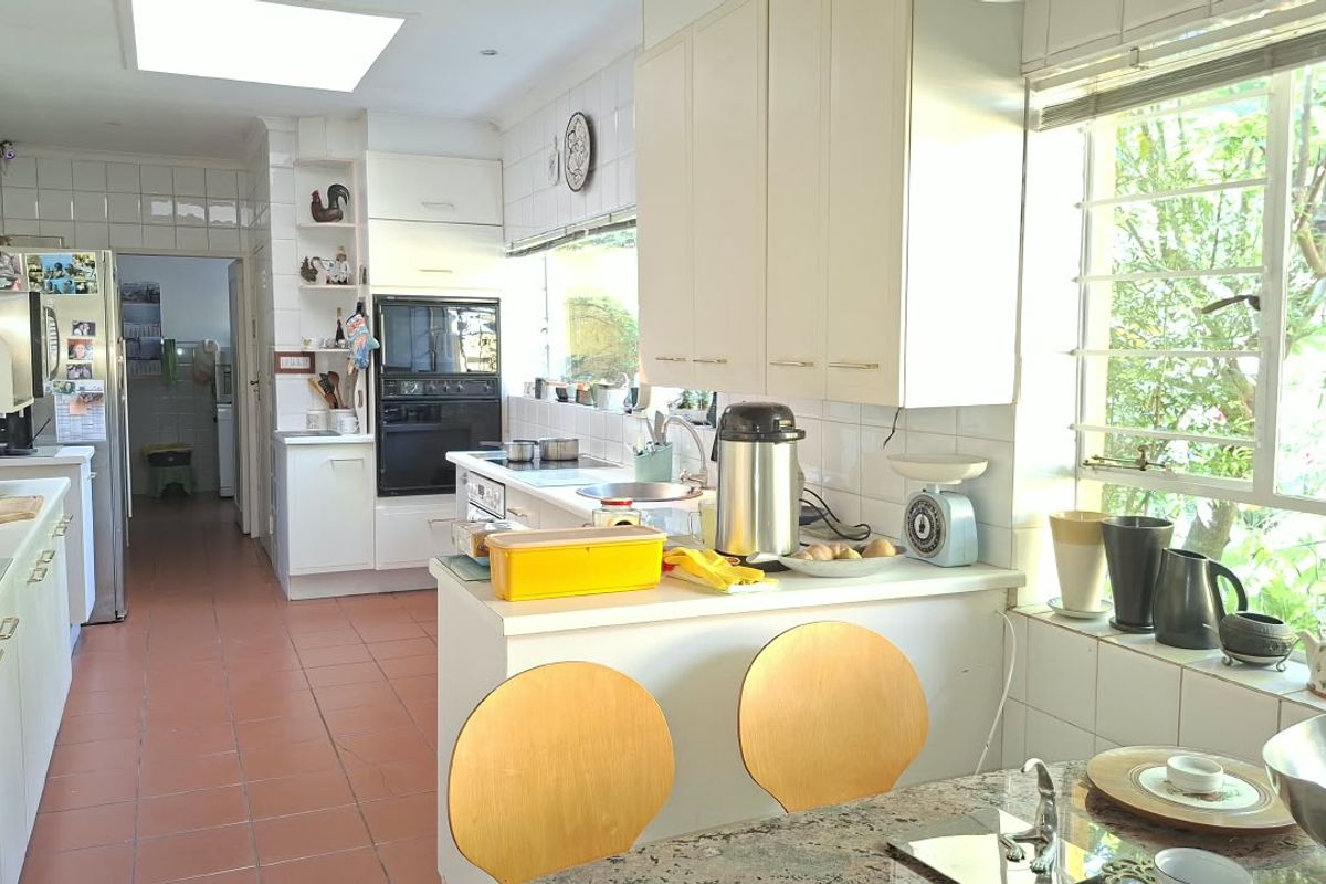 A functional kitchen featuring built-in cabinetry, integrated oven and hob, tiled splashbacks, and a skylight, offering a bright space with potential for modern updates.