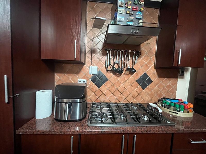 A functional kitchen area featuring dark wood cabinetry, granite countertops, a built-in gas hob, and a tiled backsplash with an integrated extractor fan.