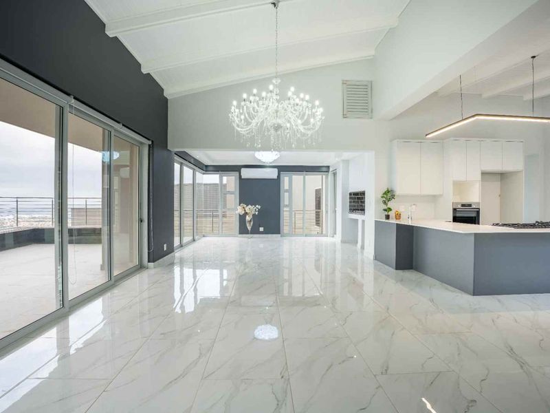 Spacious open-plan living and kitchen area featuring high vaulted ceilings, marble-look tiled flooring, modern cabinetry, and seamless access to the outdoor balcony.