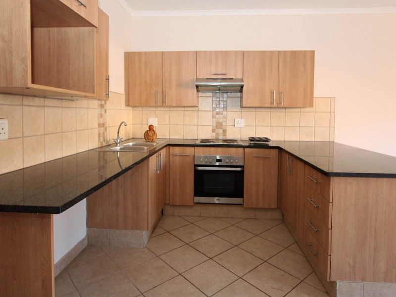 A clean, functional kitchen featuring laminate cabinetry, granite countertops, built-in oven, electric hob, and tiled backsplash.