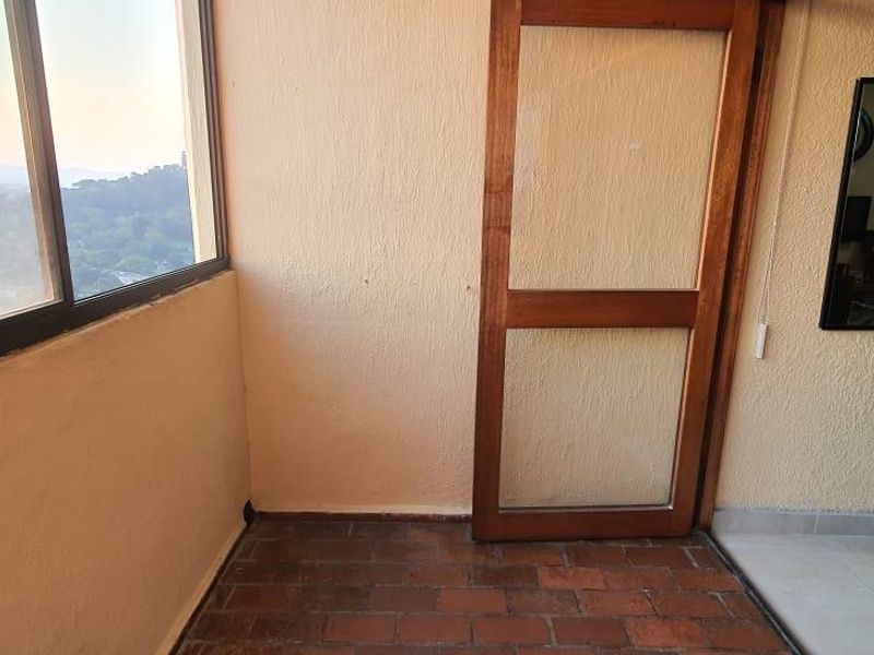 An enclosed balcony area featuring brick flooring, large windows with scenic views, and a wooden door frame leading to the interior.
