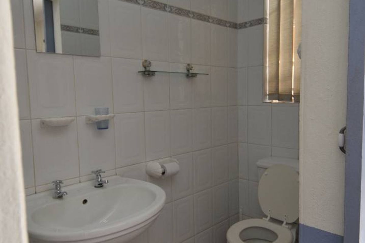 A functional bathroom featuring a pedestal basin, toilet, and tiled walls with a window for natural light.