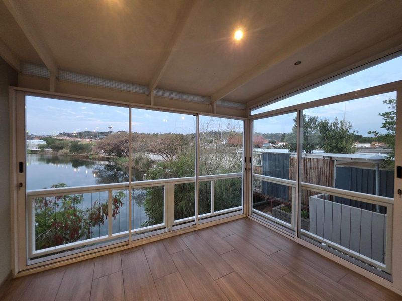 An enclosed balcony featuring modern tiled flooring, large sliding glass doors, and expansive views of the surrounding landscape and water.