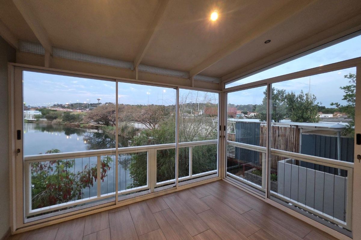 An enclosed balcony featuring modern tiled flooring, large sliding glass doors, and expansive views of the surrounding landscape and water.