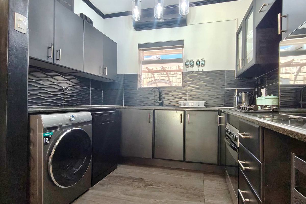 Modern kitchen featuring dark cabinetry, textured backsplash tiling, integrated oven and hob, and dedicated space for laundry appliances.
