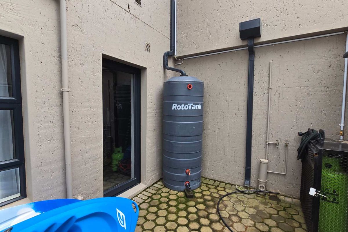 Rear exterior area featuring a grey water storage tank, downpipe system, and paved courtyard space.