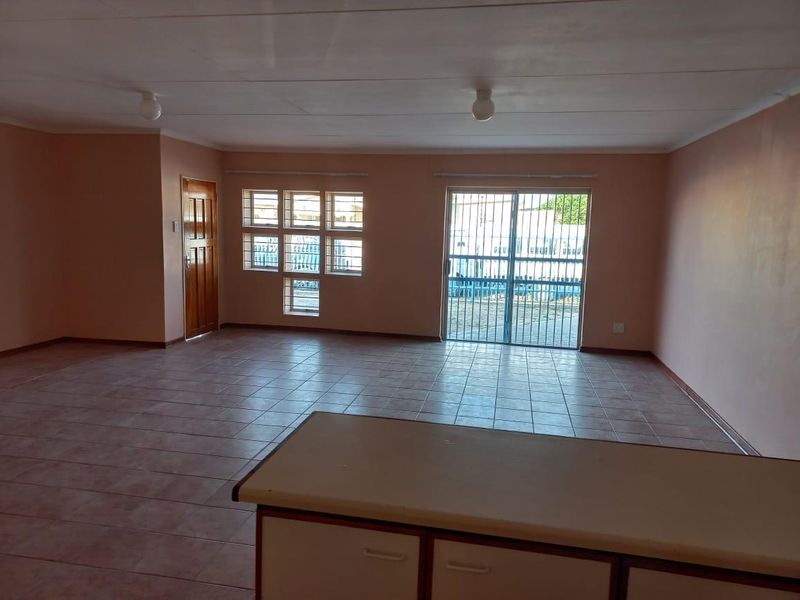 Spacious open-plan living area featuring tiled flooring, a built-in kitchen counter, and a sliding glass door with security gate leading outdoors.