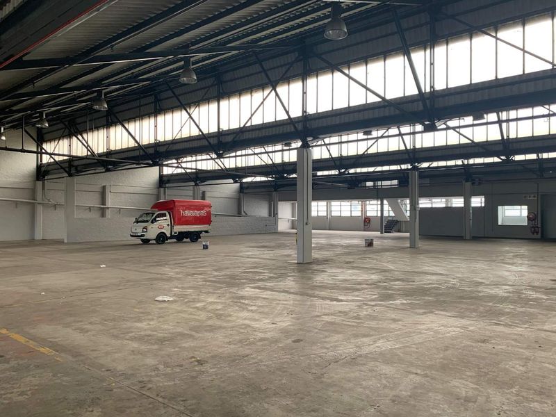 Spacious industrial warehouse featuring high ceilings with exposed steel trusses, clerestory windows for natural light, and durable concrete flooring.