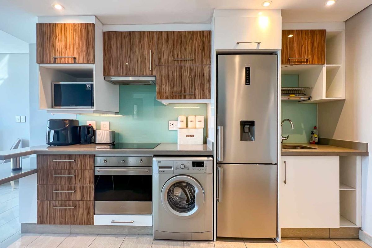 Modern kitchen featuring wood-grain cabinetry, glass splashback, integrated oven, hob, extractor fan, and built-in space for a washing machine and refrigerator.