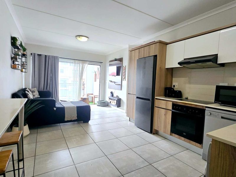 Modern open-plan living area featuring a contemporary kitchen with built-in appliances, tiled flooring, and direct access to a balcony through sliding glass doors.