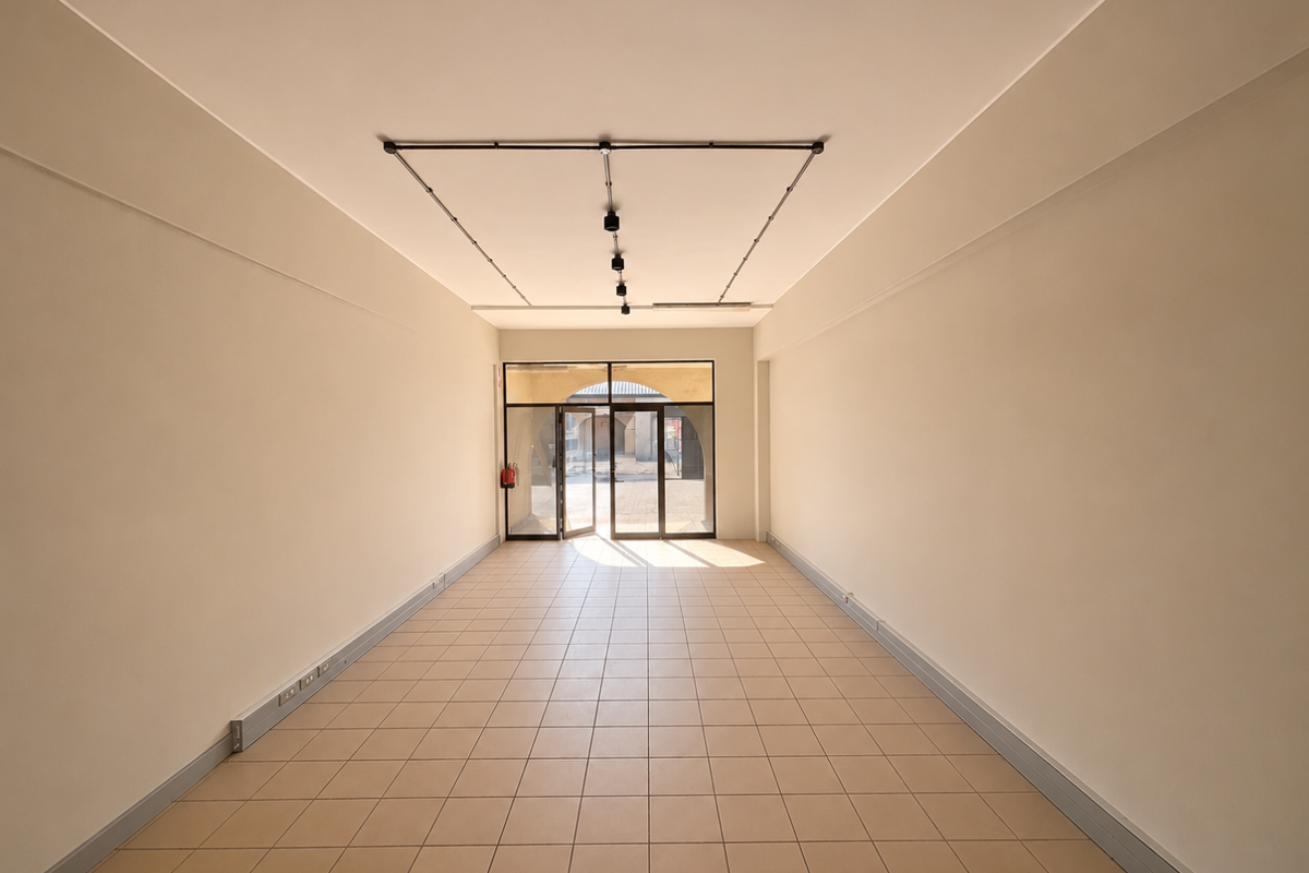 A bright, empty retail space featuring ceramic tile flooring, track lighting, and a glass entrance door, suitable for various commercial business applications.