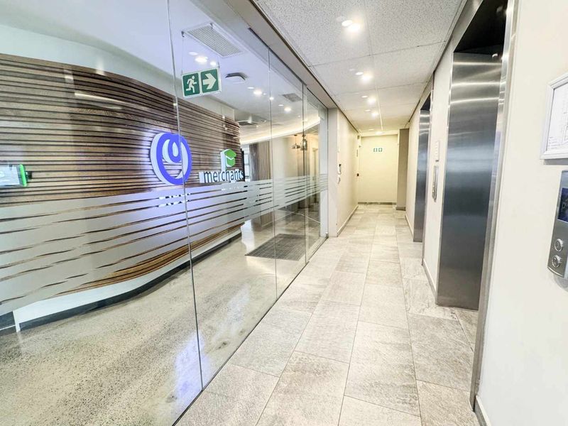 A modern commercial office hallway featuring stone flooring, a glass partition wall, timber slat detailing, and stainless steel elevator access.