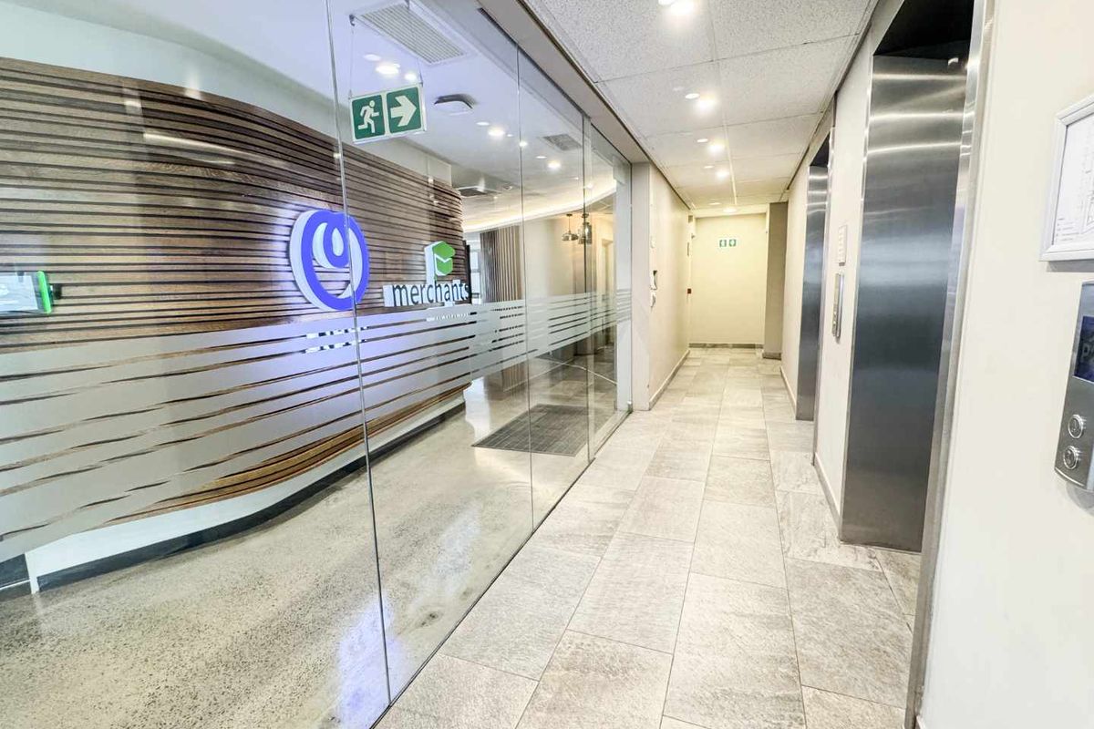 A modern commercial office hallway featuring stone flooring, a glass partition wall, timber slat detailing, and stainless steel elevator access.