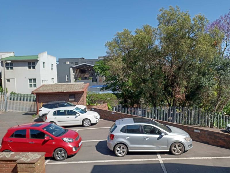 Rear exterior view of the office property featuring an asphalt parking area, brick retaining wall, and steel palisade fencing.