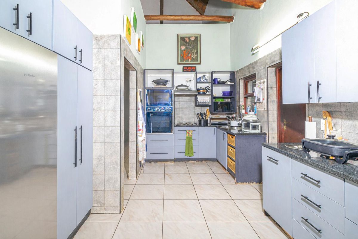 A functional kitchen featuring light blue cabinetry, granite countertops, tiled flooring, and exposed timber ceiling beams.