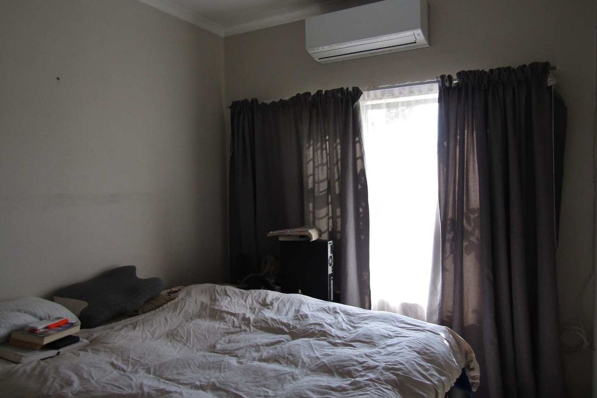A bedroom featuring a wall-mounted air conditioning unit and a window with curtain tracks.
